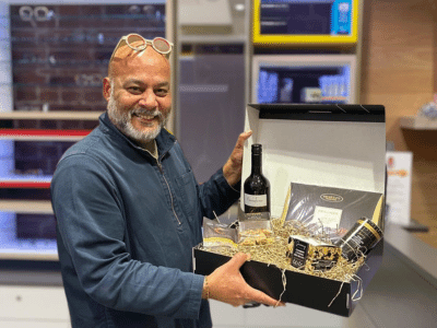 a man with his glasses on his head smiling whilst holding a hamper raffle prize