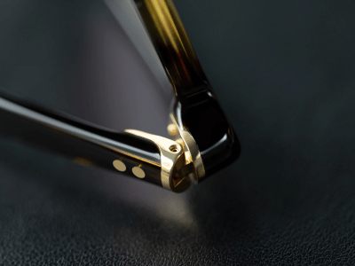 close up image of the hinge on a lunor glasses frame that highlights the smooth curved and polished edge of the frame and golden hinge fitted seamlessly