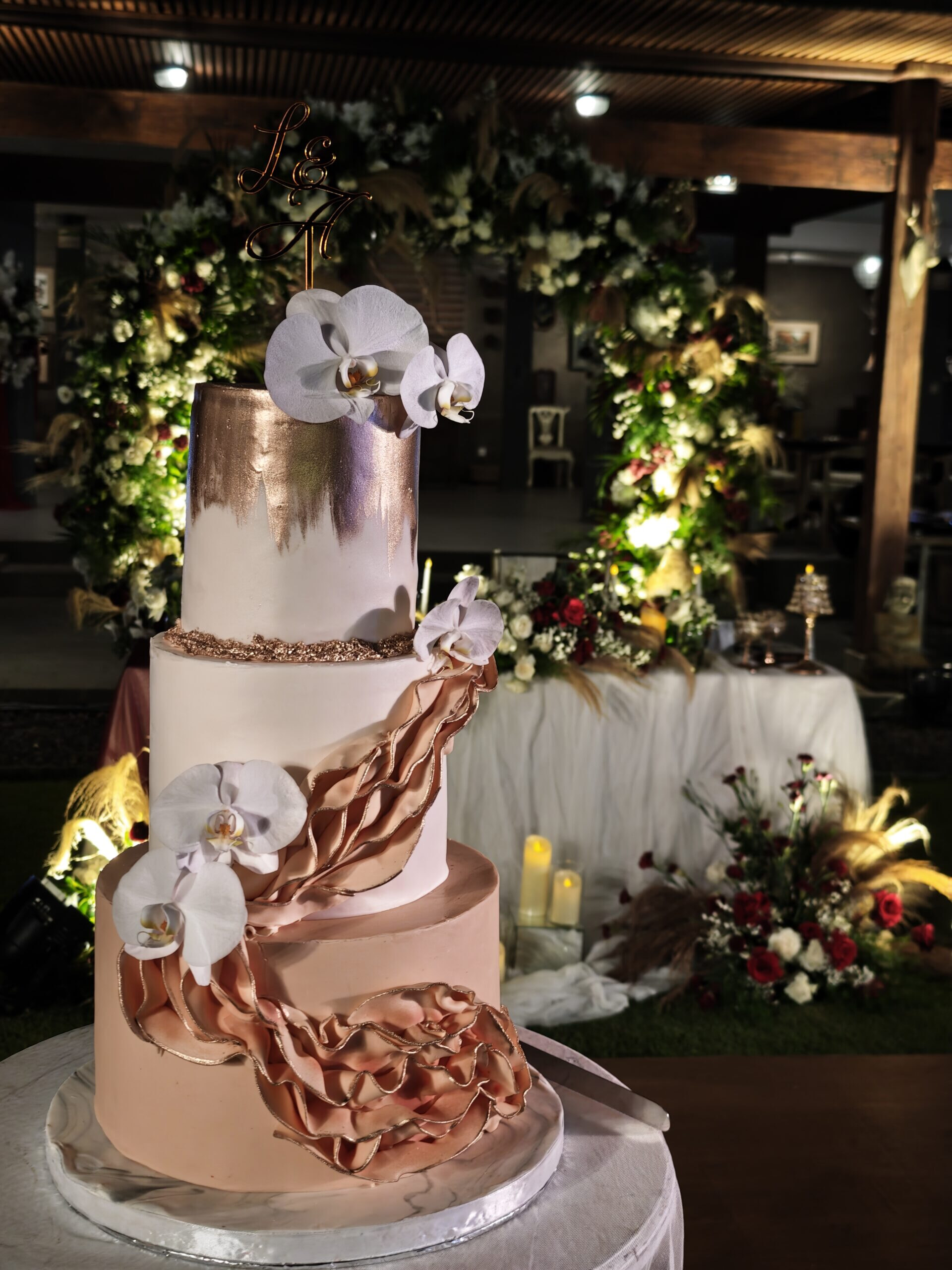 image of a tall 3 tier cream cold and burnt orange wedding cake with orchids and flowing design