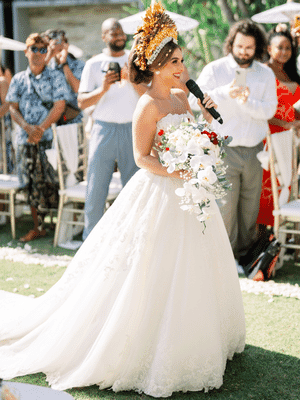 image of a singing bride wearing a Vera Wang - Ballgown white dress with lace embelishments. The bride is walking down the isle alone whilst singing to the congregation. the bride is wearing Gelungan Payas Agung royal headress