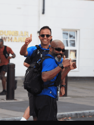 two men wearing matching blue shirts and black shorts both with thumbs up happy expressions running