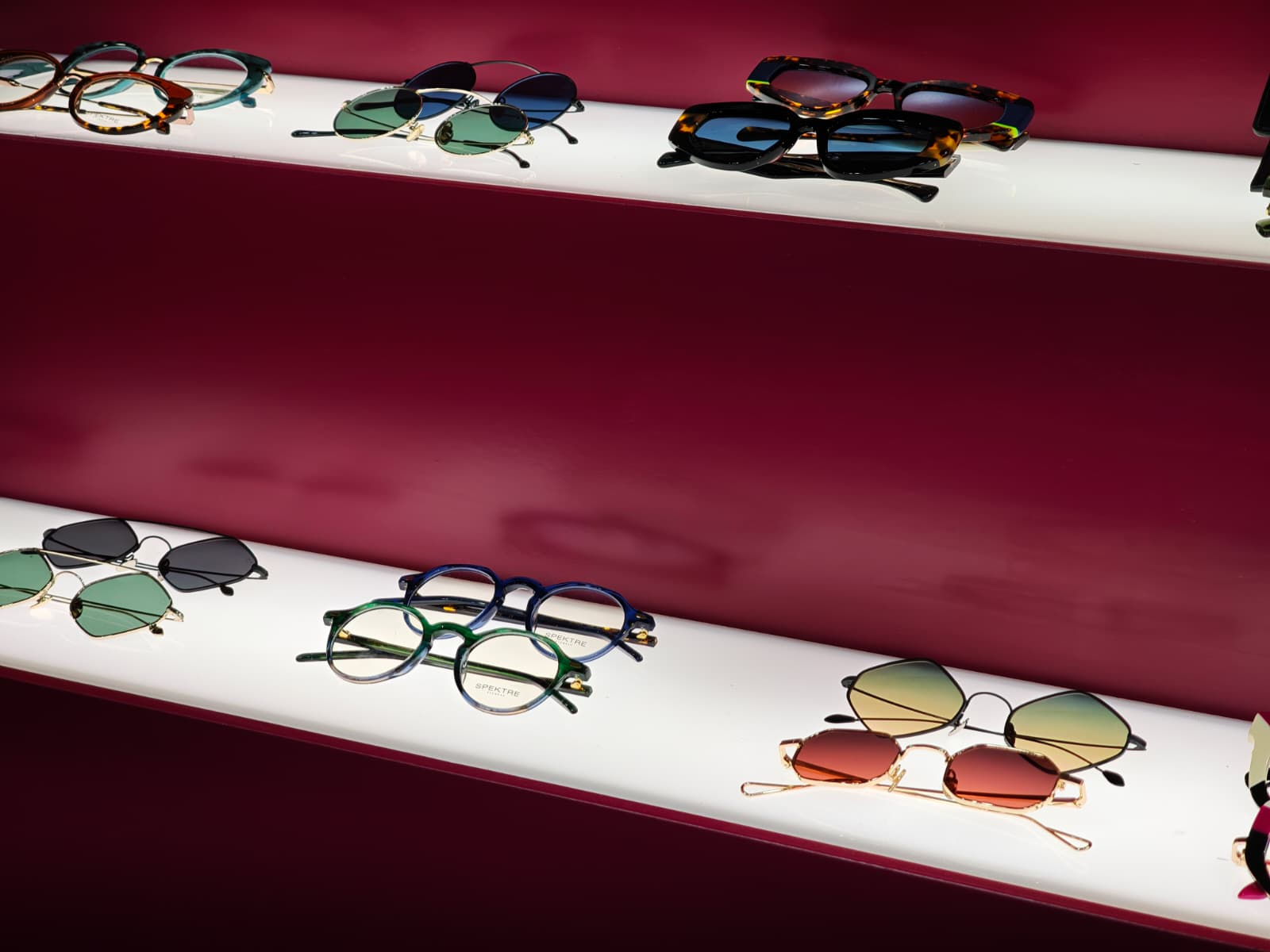 A display of colourful designer sunglasses and optical frames on illuminated white shelves against a deep magenta wall at SILMO Paris 2025.