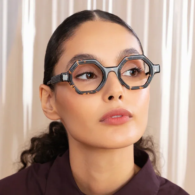 Close-up of a woman wearing geometric tortoiseshell octagonal eyeglasses, looking slightly upward against a neutral backdrop.